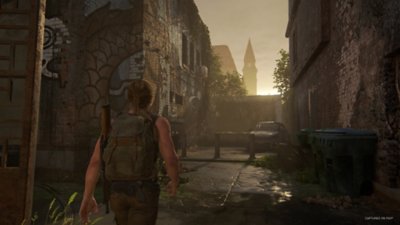 The Last of Us Part II Remastered screenshot showing Abby walking through a town towards a sunset